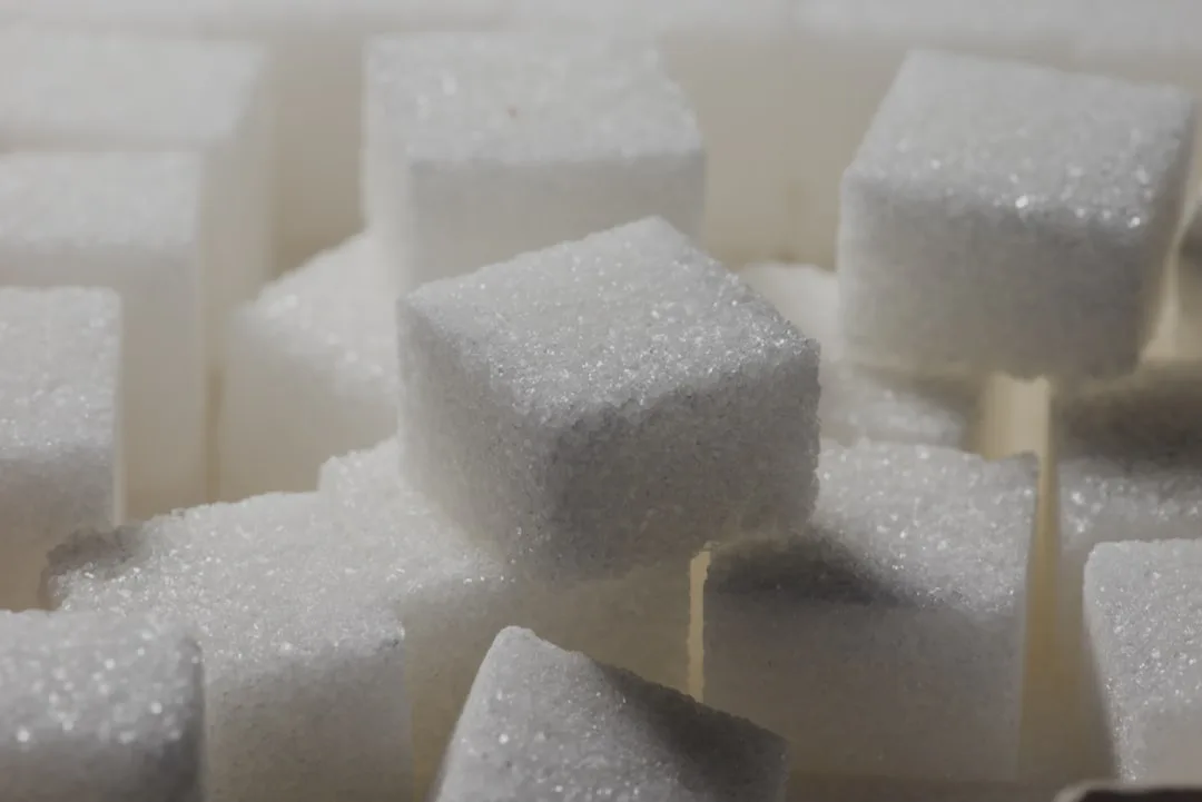 Una mano sosteniendo un terrón de azúcar junto a caramelos sin azúcar de Beneo, con un fondo abstracto que representa la economía y la innovación.